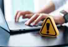 Fake websites are impersonating 100 popular brands in large-scale scam campaign Warning scam sign placed on a table while person works